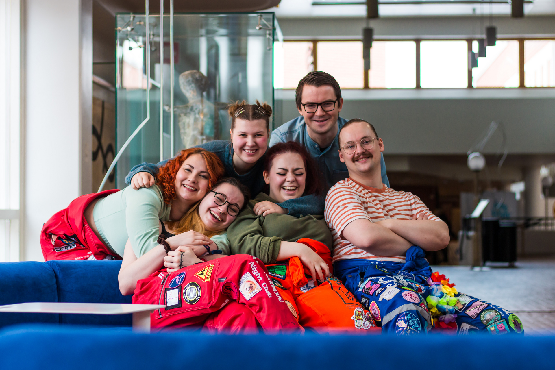 Six smiling and laughing students sit close together on a blue couch.