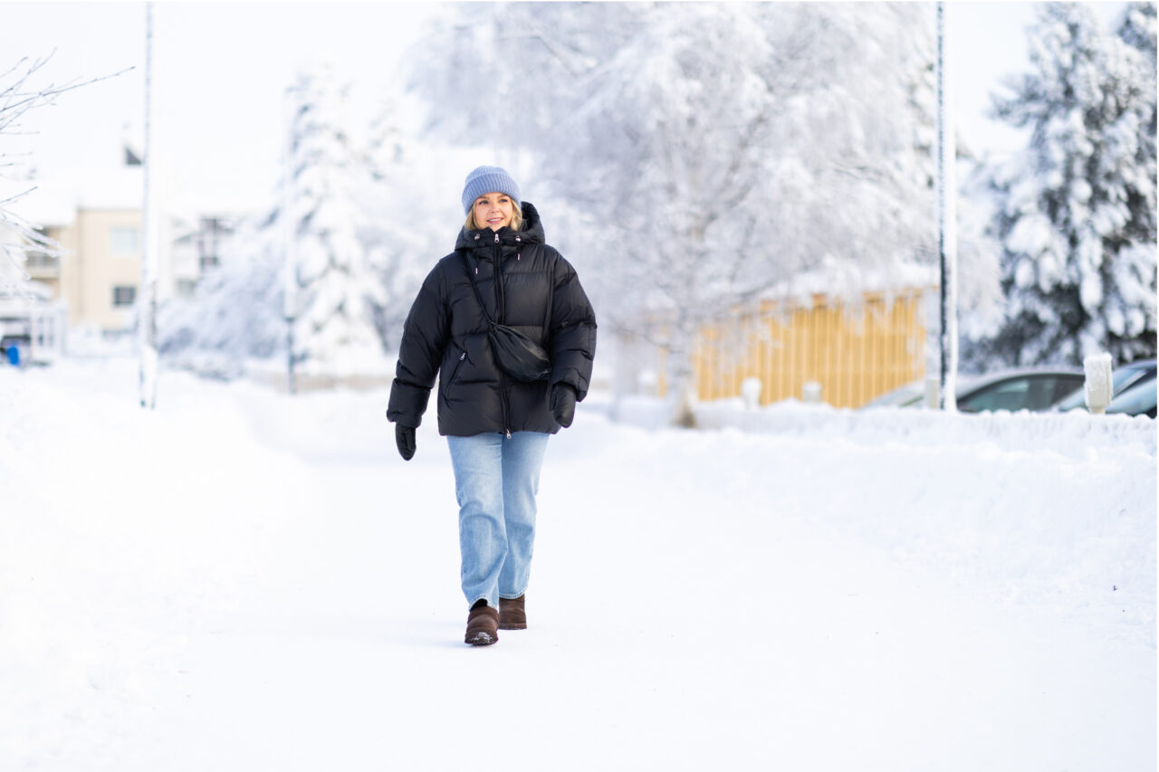 Toppatakkinen nainen kävelee lumimaisemassa.