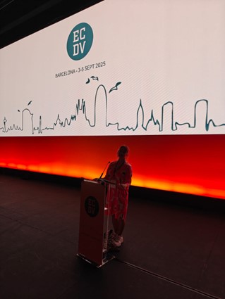 Kuva Nenna Jyläskoskesta, joka pitää puhujakorokkeeen takaa tieteellistä esitystä European Conference on Domestic Violence (ECDV) -konferenssissa.
