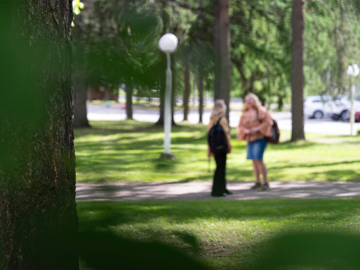 Kaksi opiskelijaa seisoo juttelemassa puistossa.