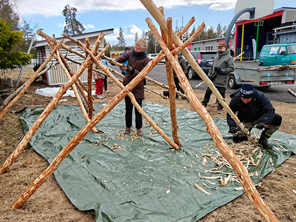 Kolme henkilöä asettelee koivurankoja luovviin.