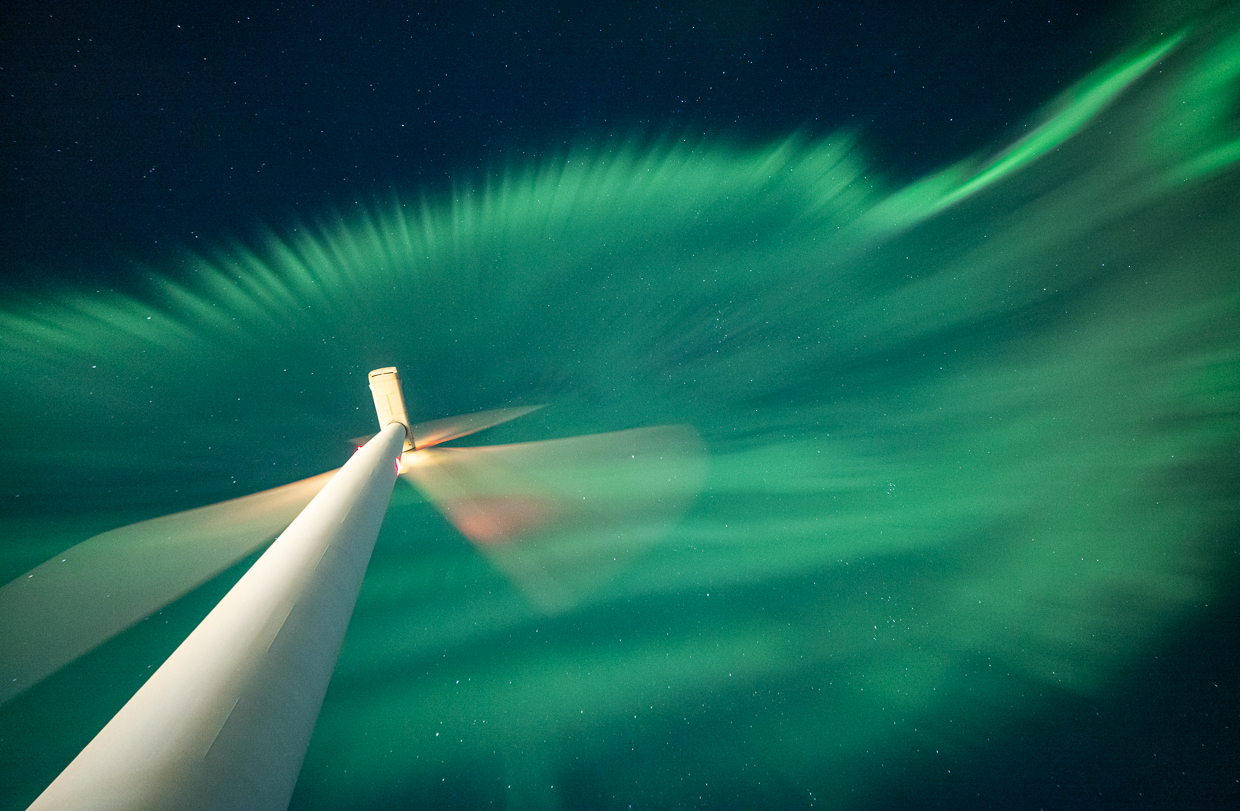 Esa Pekka Isomursun teos Solar Wind Power. Teoksessa etualalla alaviistosta kuvatun tuulivoimalan lapojen liike taustallaan taivaalla olevien revontulten värit.