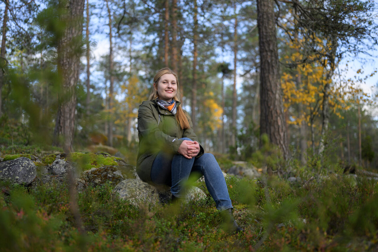 Karolina Sikora istuu kiven päällä metsässä.
