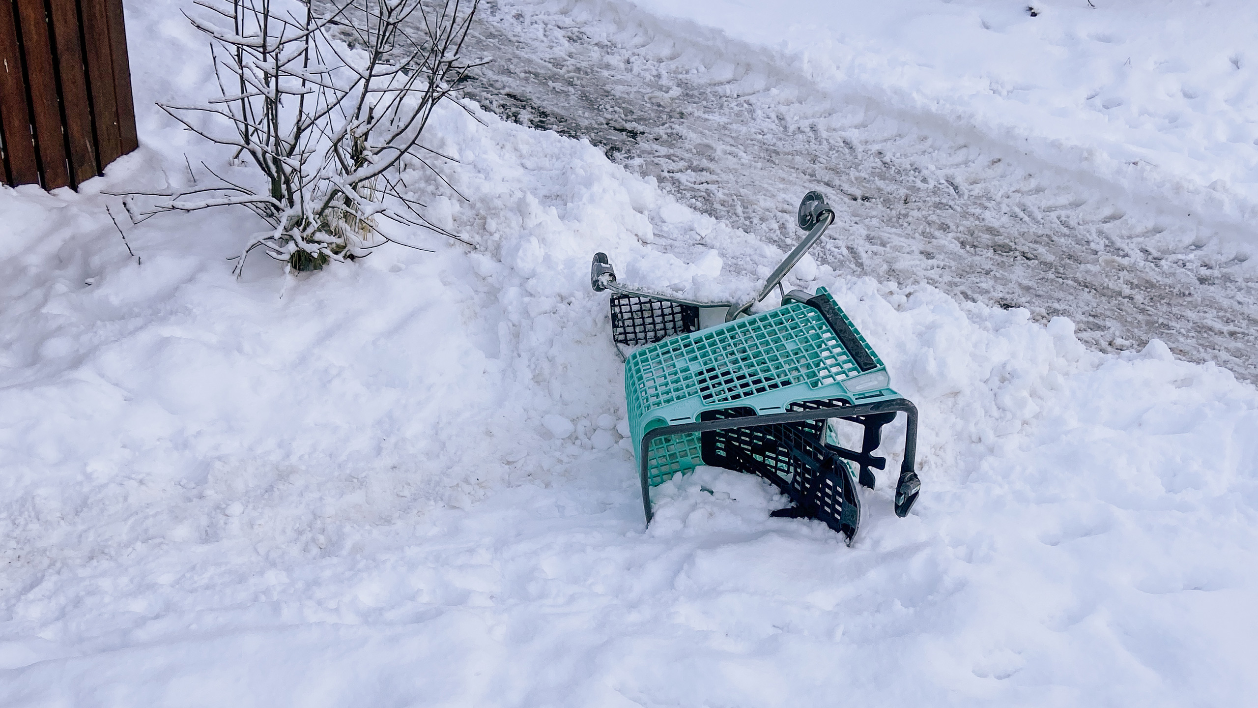 Vihreä ostoskärry kumollaan lumessa.