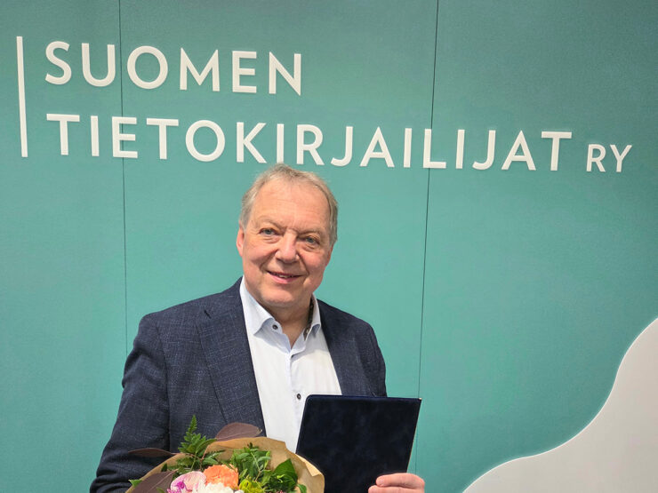 Palkittu Markku Heikkilä onnittelukirjan ja kukkien kanssa.
