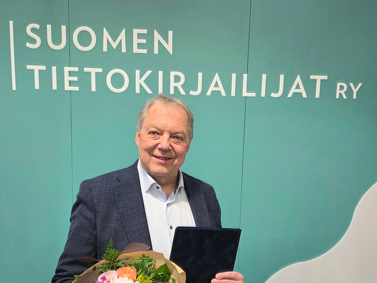 Palkittu Markku Heikkilä onnittelukirjan ja kukkien kanssa.