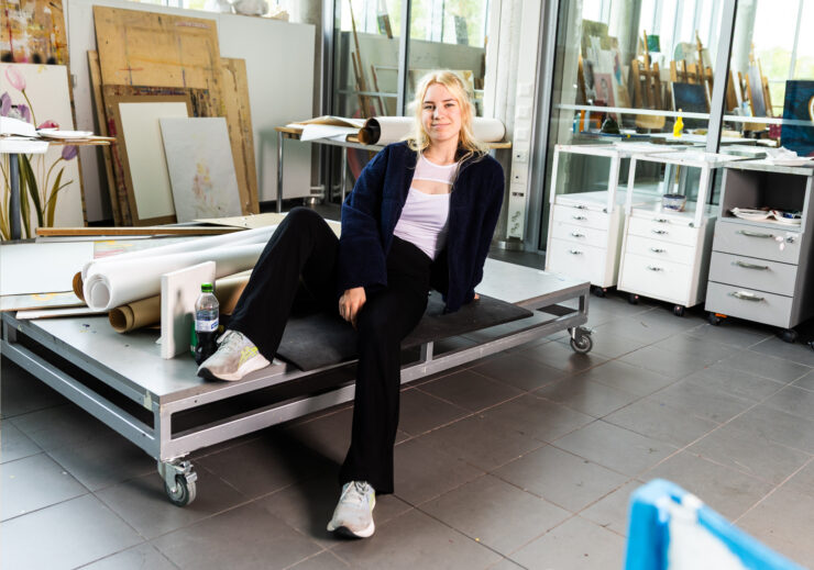 Kuvataidekasvatuksen opiskelija istuu rullakon päällä taideateljeessa.