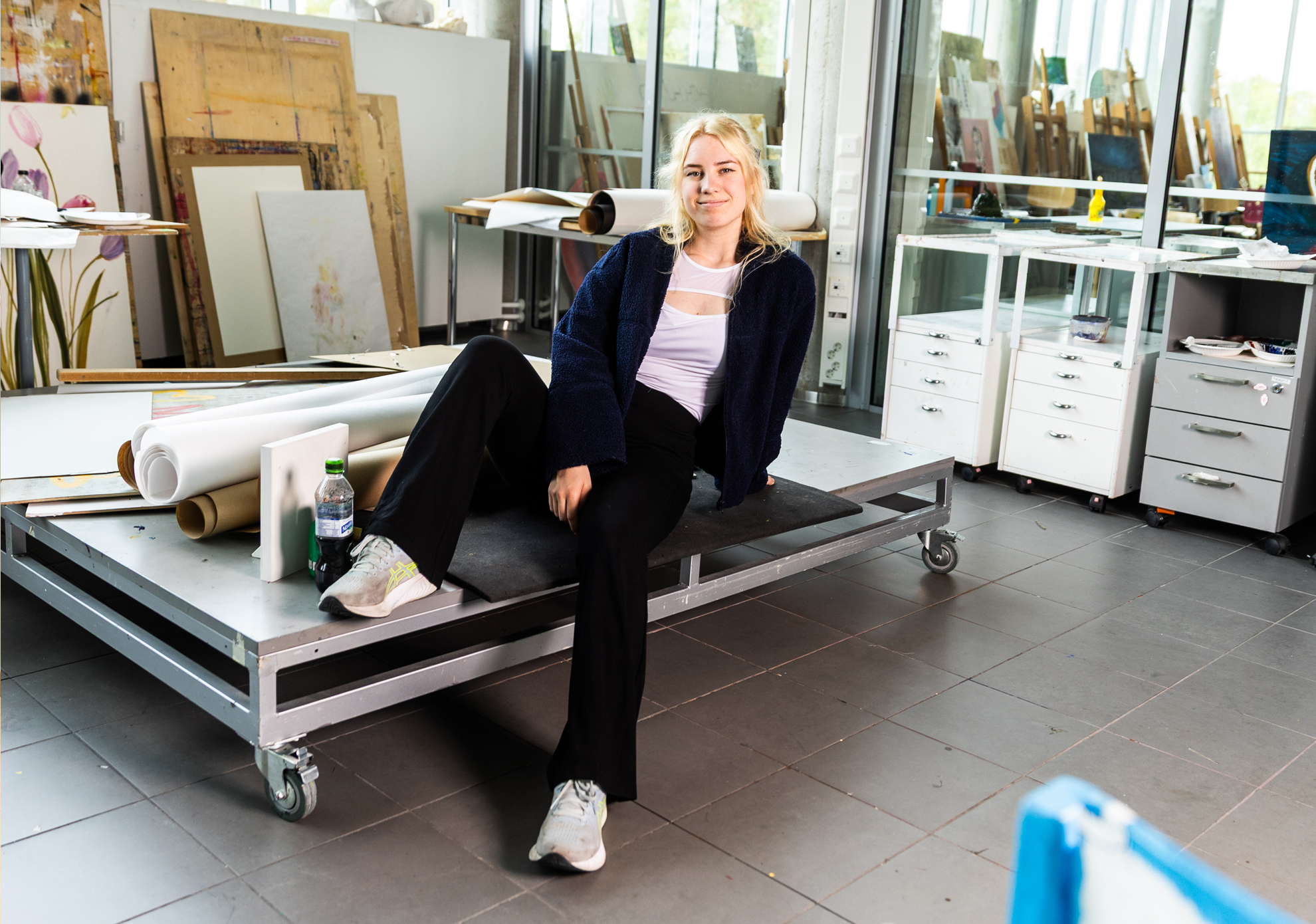 Kuvataidekasvatuksen opiskelija istuu rullakon päällä taideateljeessa.